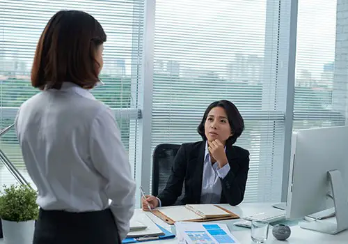 a businesswoman sitting at her desk talking to a female employee.