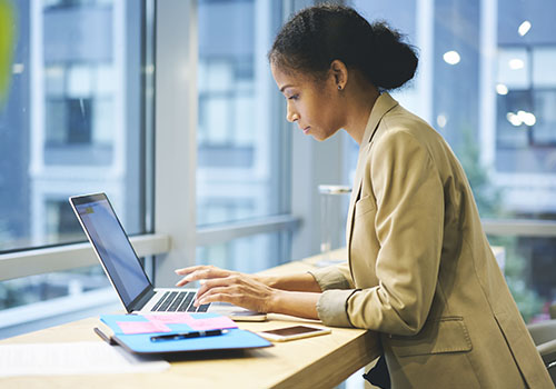 A female in a modern workspace, concentrating on writing emails to coworkers.