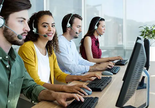 A group of employees at a call center in front of their computers with headphones on.