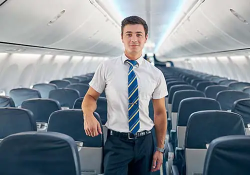 Young flight attendant standing in the aisle of an aircarft and smiling.