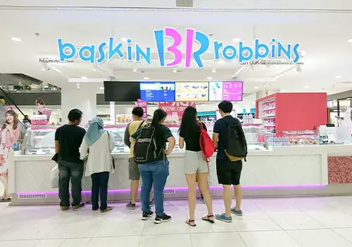a group og people standing in amodern, well lit Baskin Robbins store.