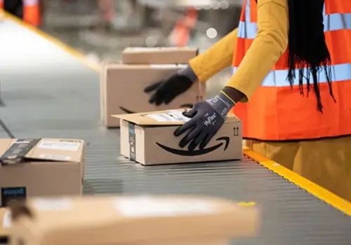 An Amazon warehouse worker moving a small box along the conveyer belt