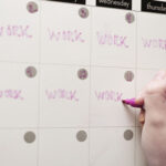 Female handwriting on a a calendar whiteboard filled with a busy work schedule.