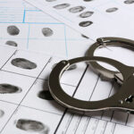 A pair of handcuffs on top of fingerprint record sheets.